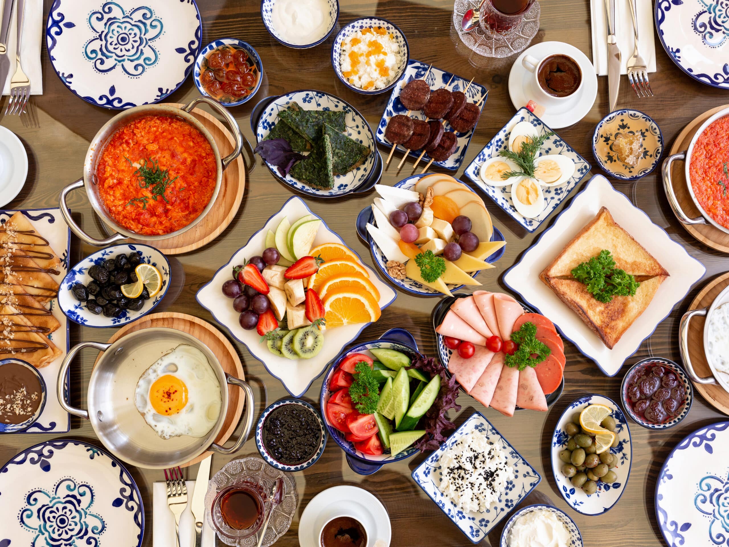 top view of set of various plates of food for breakfast fried eggs with tomatoes fruit salad ham vegetables cheese toasts on rustic background